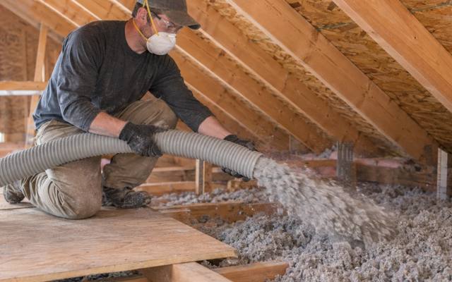 Worker blowing grey loose-fill insulation between attic joists after insulation removal
