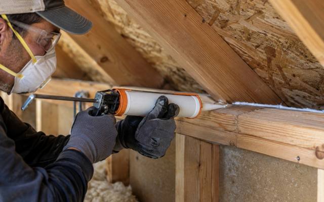 Worker caulking a joint along the top of an attic wall before new insulation goes in
