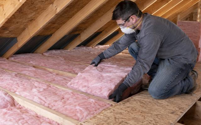 Worker kneeling on an attic floor handling pink fibreglass batts in a St. Thomas house
